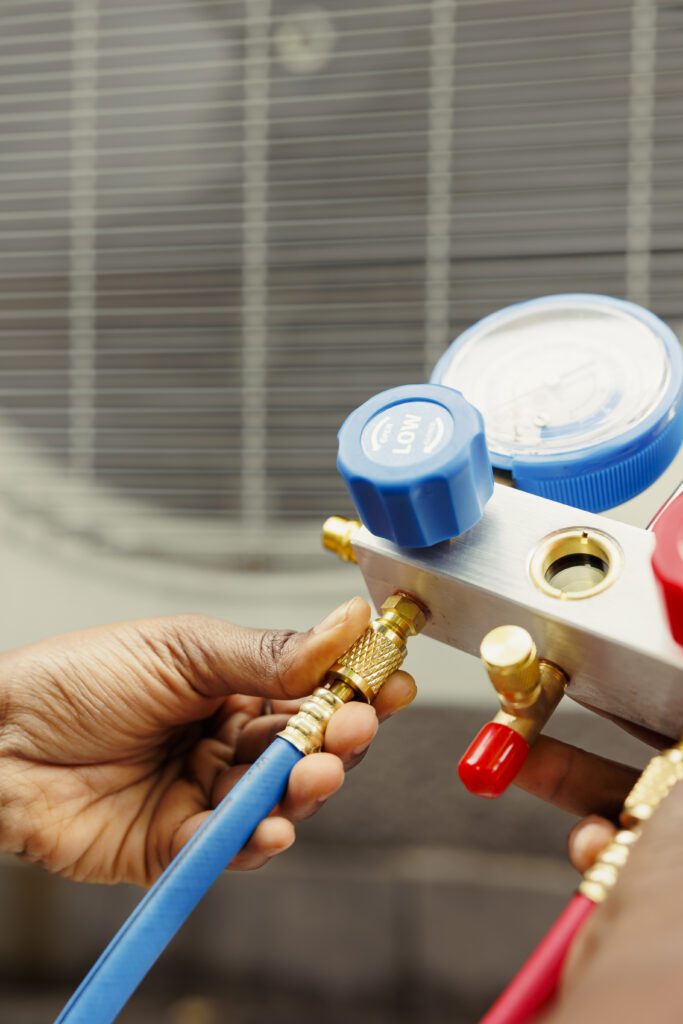 Close up of professional worker holding pressure indicators used for checking air conditioner freon tank in need of maintenance. Licensed serviceman using manifold gauges to check refrigerant levels